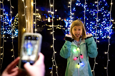 An evening image of a young girl posing for a photo next to multicolored lights.